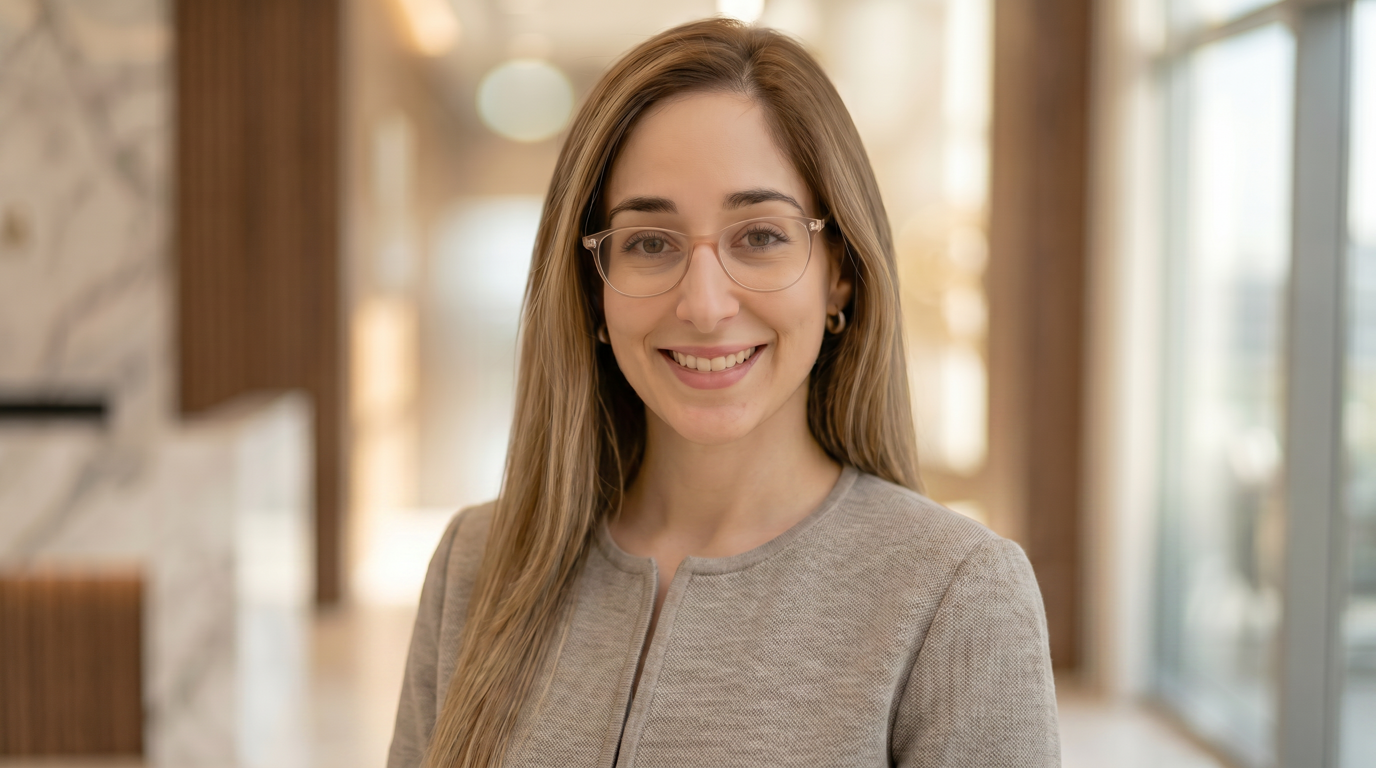 Woman with glasses smiling in a blurred indoor setting